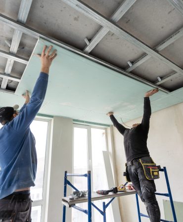 Workers fitting panel into frame of ceiling.